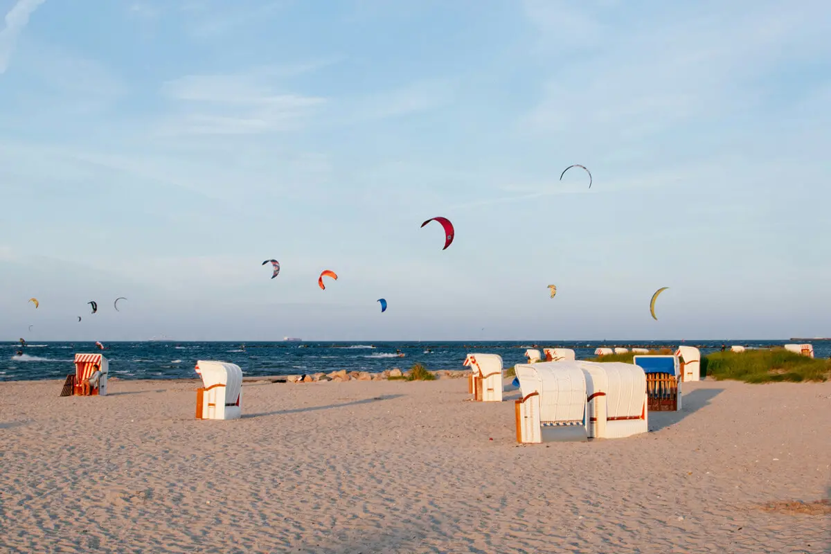Sandstrand auf Fehmarn mit weißen Strandkörben und bunten Kites am Himmel über dem Meer.