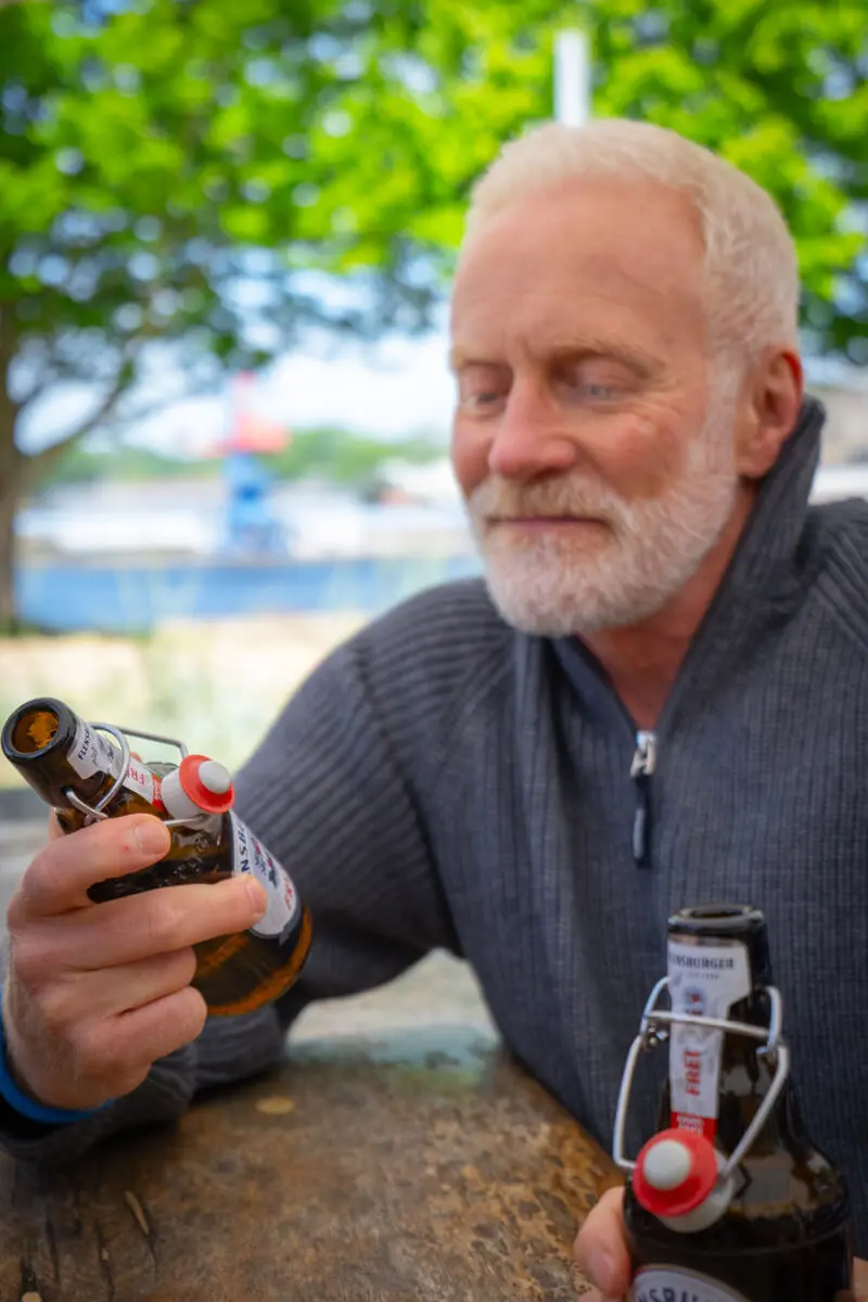 Andreas Arndt hält FLENS Bierflasche mit Bügelverschluss in der Hand und guckt sich das Etikett an.