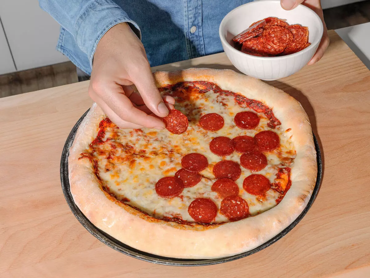 Pizza, die mit Salami belegt wird.