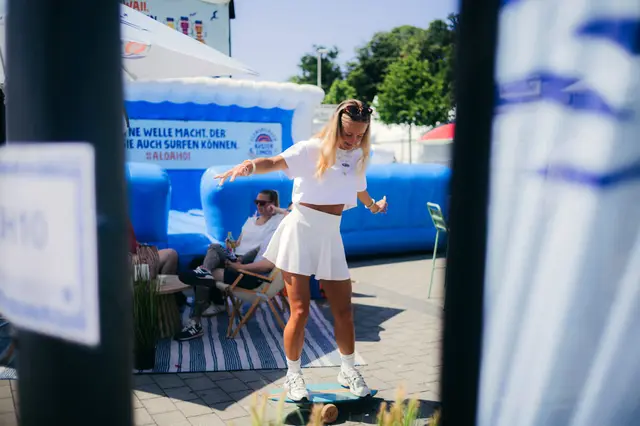 Frau balanciert auf Balanceboard bei der Kieler Woche 2025 vor blauen Inflatable-Strukturen.