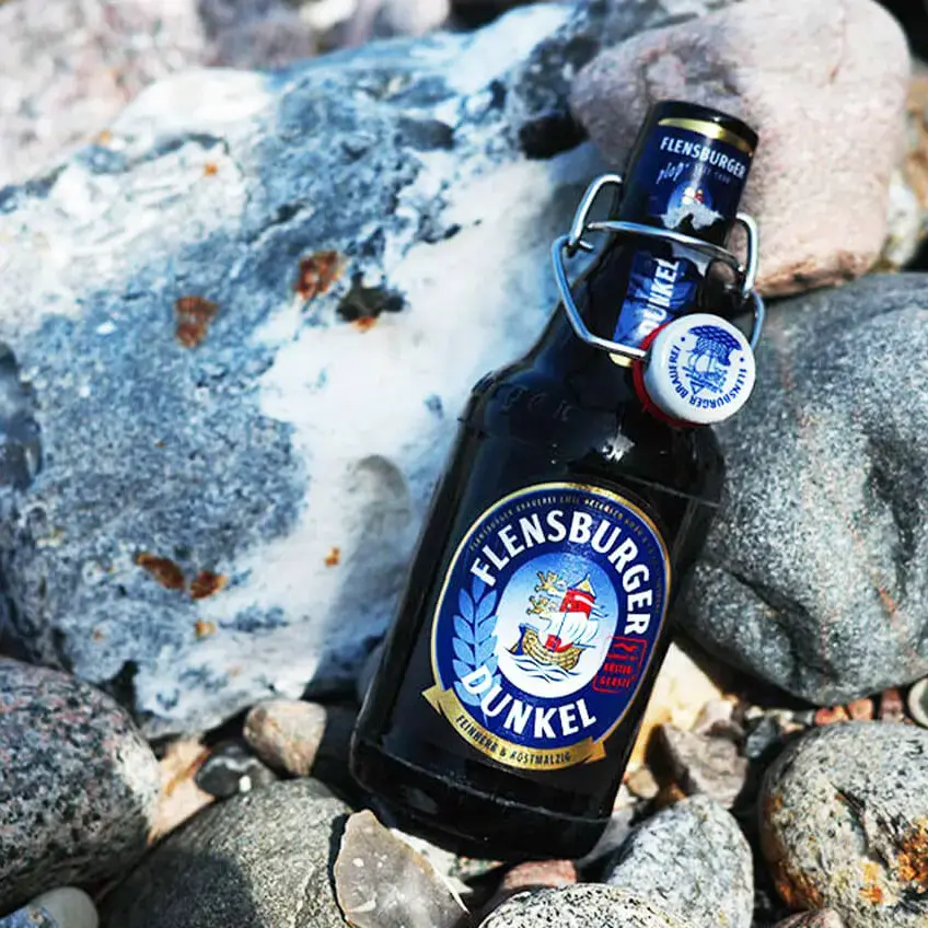 Flensburger-Dunkel-Bierflasche auf kiesigen Strandfelsen.