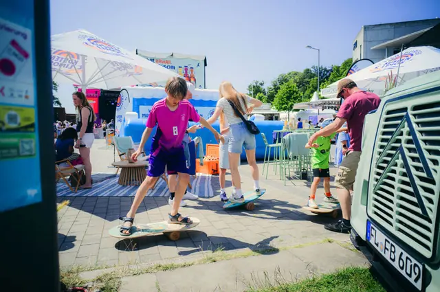 Kieler Woche 2025 mit Kindern beim Testen der Balance-Boards unter Sonnenschirmen auf Festivalgelände.