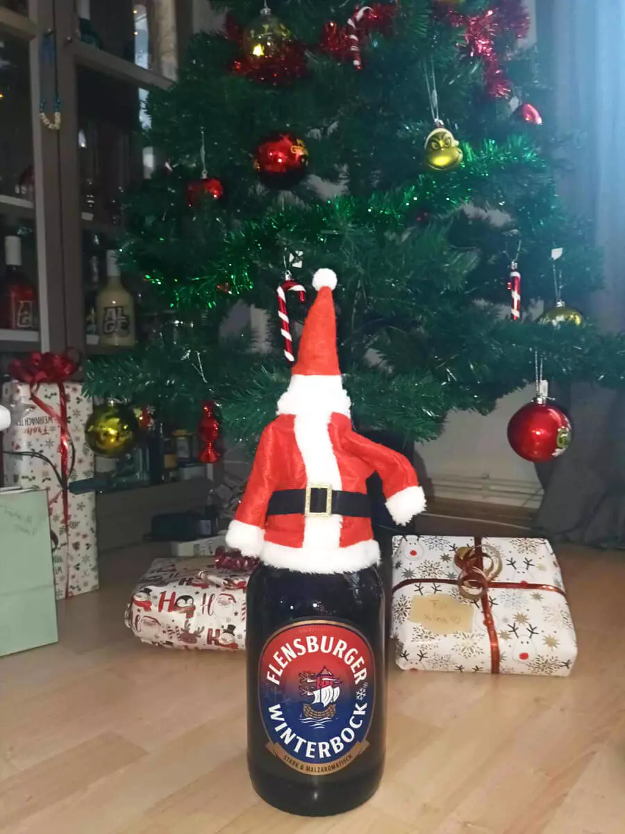 Der Flensburger Winterbock mit Weihnachtsmanndeko, im Hintergrund eine Tannenbaum mit Geschenken.
