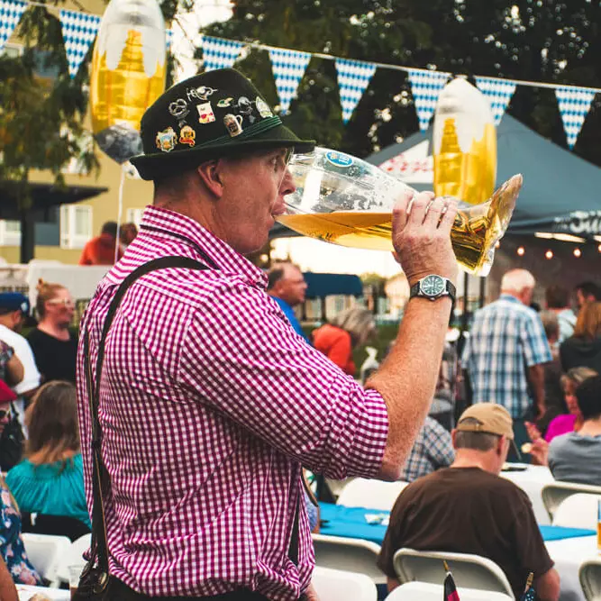 Mann auf dem Oktoberfest trinkt Bier aus einem stiefelförmigen Glas.